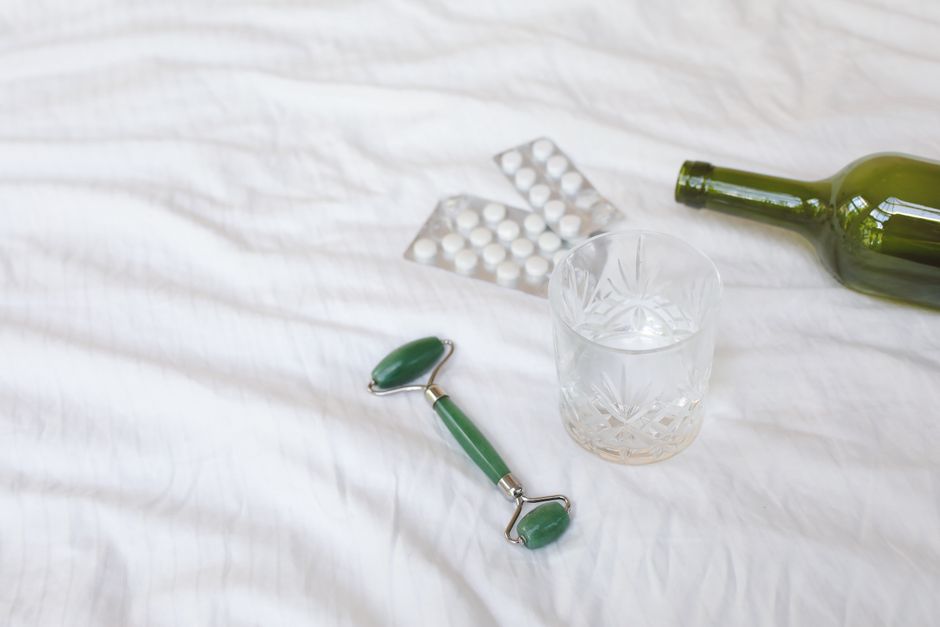A jade roller, empty glass, bottle, and tablets arranged on a soft white surface.